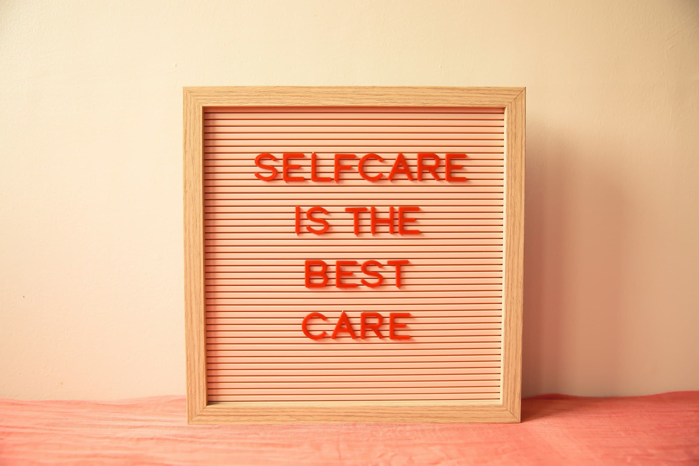 Panneau en bois avec le texte "SELFCARE IS THE BEST CARE" en lettres rouges, soulignant l'importance du bien-être personnel.